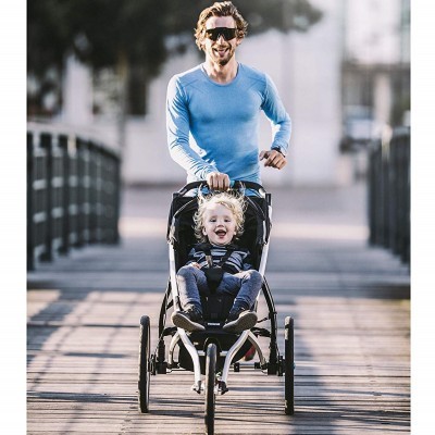 Carrinho de criança preto com três rodas e criança sentada, homem a empurrar no passadiço de madeira ao ar livre