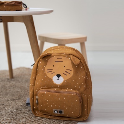 Mochila castanha com rosto de tigre e padrão de traços brancos numa sala com mesa e banco de madeira