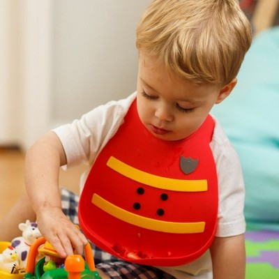 Criança com babete vermelho e amarelo a brincar com brinquedos