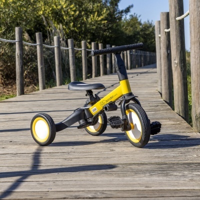 triciclo infantil amarelo e preto numa passadeira de madeira ao ar livre