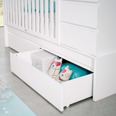 Berço branco com gaveta aberta contendo almofadas coloridas e caixa branca