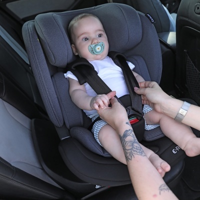Bebé numa cadeira auto cinza escuro com cinto de segurança preto instalada dentro de um carro