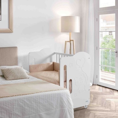 Berço branco ao lado de cama de casal numa sala clara com janela aberta