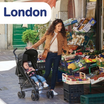 Mulher a empurrar carrinho de bebé preto junto a banca de frutas e legumes