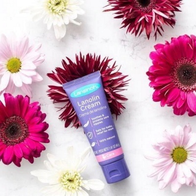 Tube de Lanolin Cream lilás claro rodeado por flores vermelhas e rosas sobre fundo branco