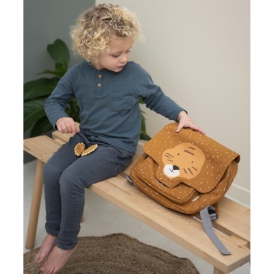 Criança sentada com mochila castanha decorada com rosto de tigre.