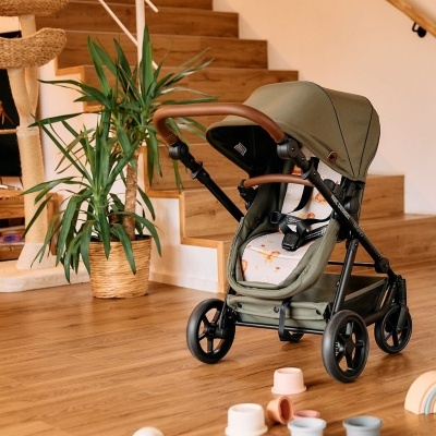 Carrinho de bebé verde em ambiente interior com chão de madeira e planta