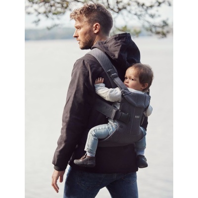 Homem com bebé em canguru cinzento junto a água