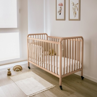 Berço de bebé de madeira clara com colchão branco e padrão de estrelas numa sala clara com tapete e quadros na parede