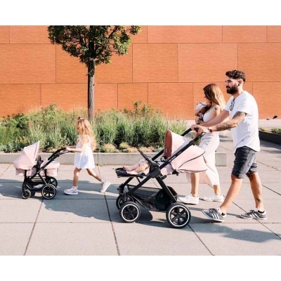Carrinho de bebé rosa claro com estrutura preta em passeio ao ar livre.
