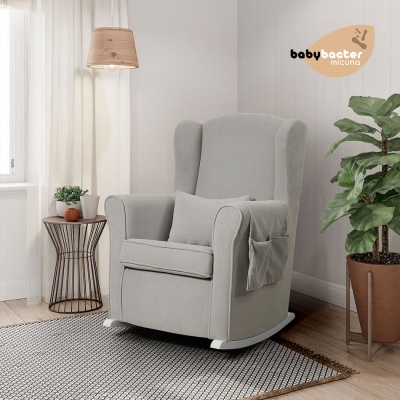 Cadeira de amamentação cinza claro numa sala com planta, tapete e candeeiro
