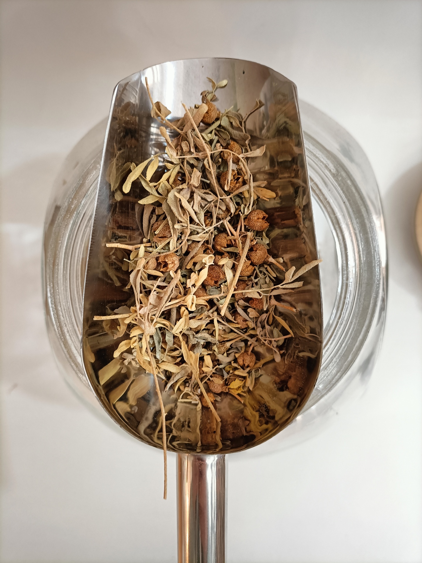 Arruda GRANEL Concha metálica prateada com mistura de folhas secas sobre frasco branco