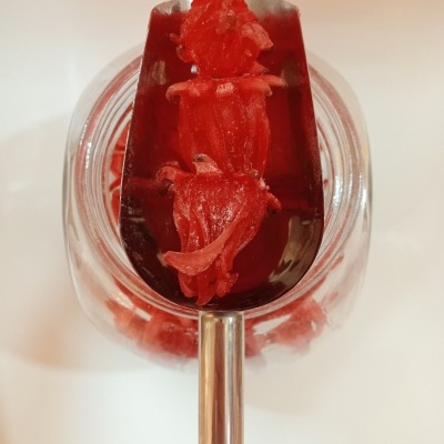 Flor de Hibisco Cristalizada GRANEL Colher metálica com flores vermelhas dentro de frasco transparente