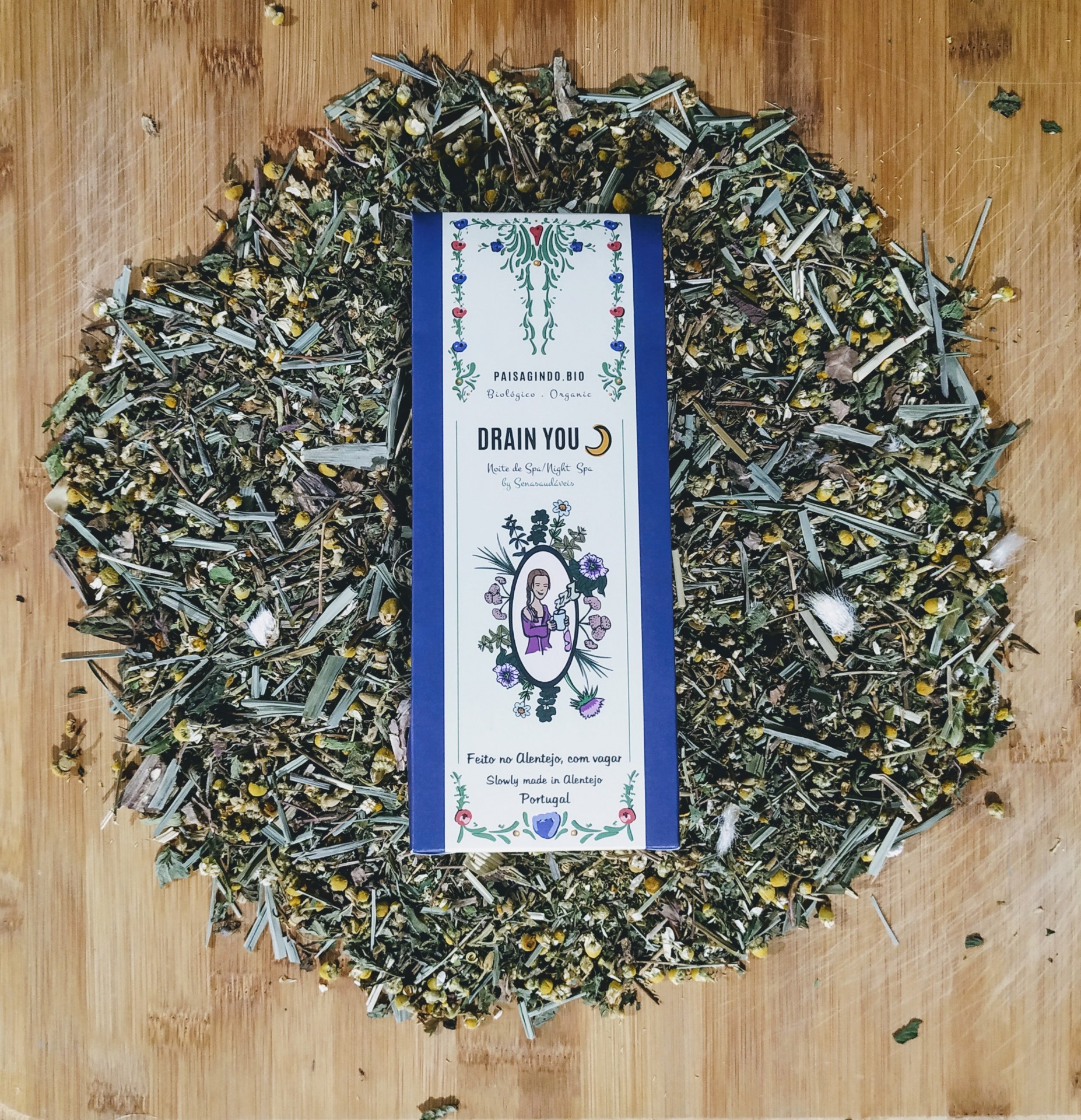 Infusão Drain You (Noite) Paisagindo 40g Saco de chá herbal DRAIN YOU com ilustração floral, rodeado por ervas soltas sobre tábua de madeira