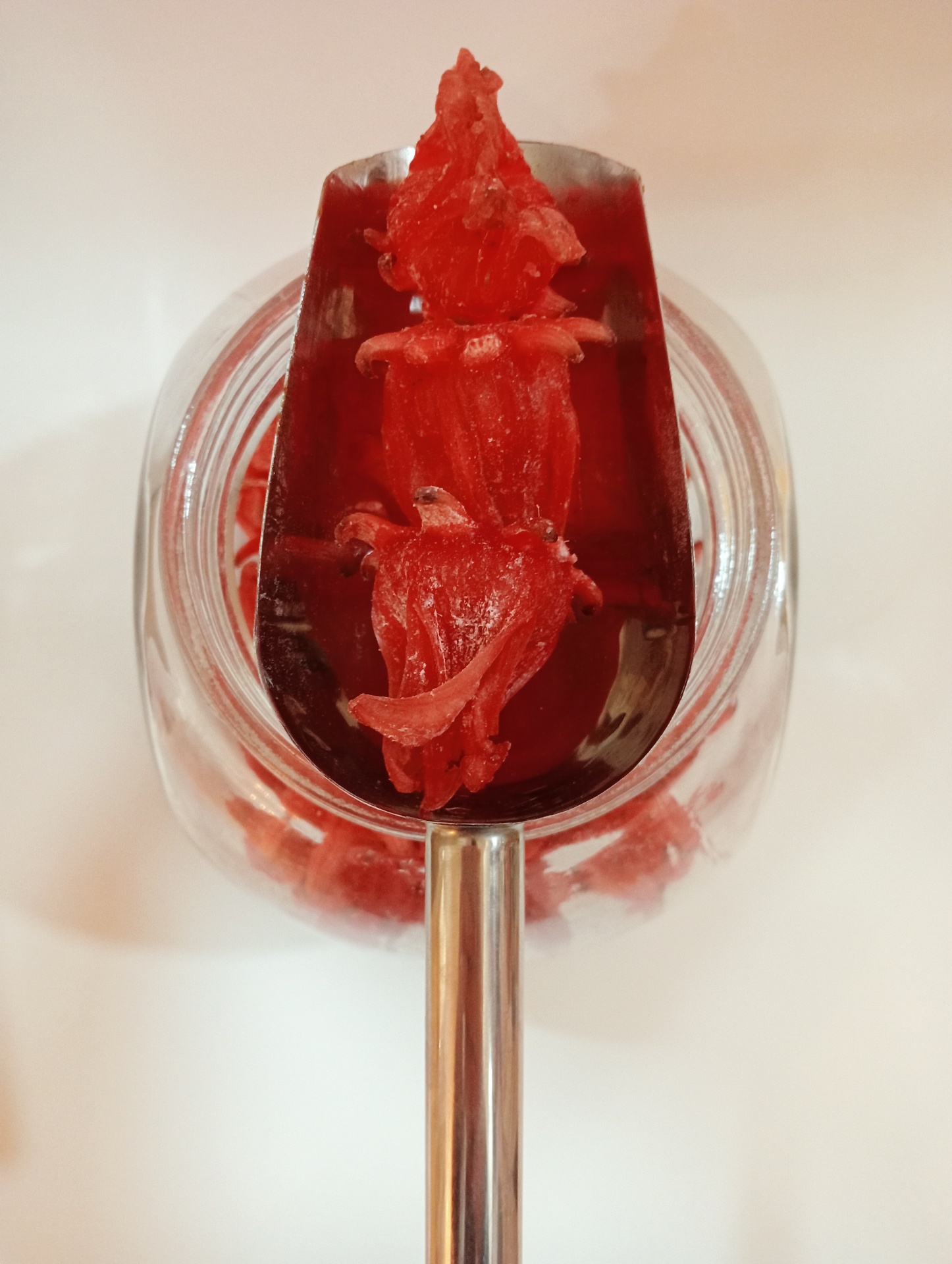 Flor de Hibisco Cristalizada GRANEL Colher de metal com flores vermelhas em conserva dentro de frasco de vidro