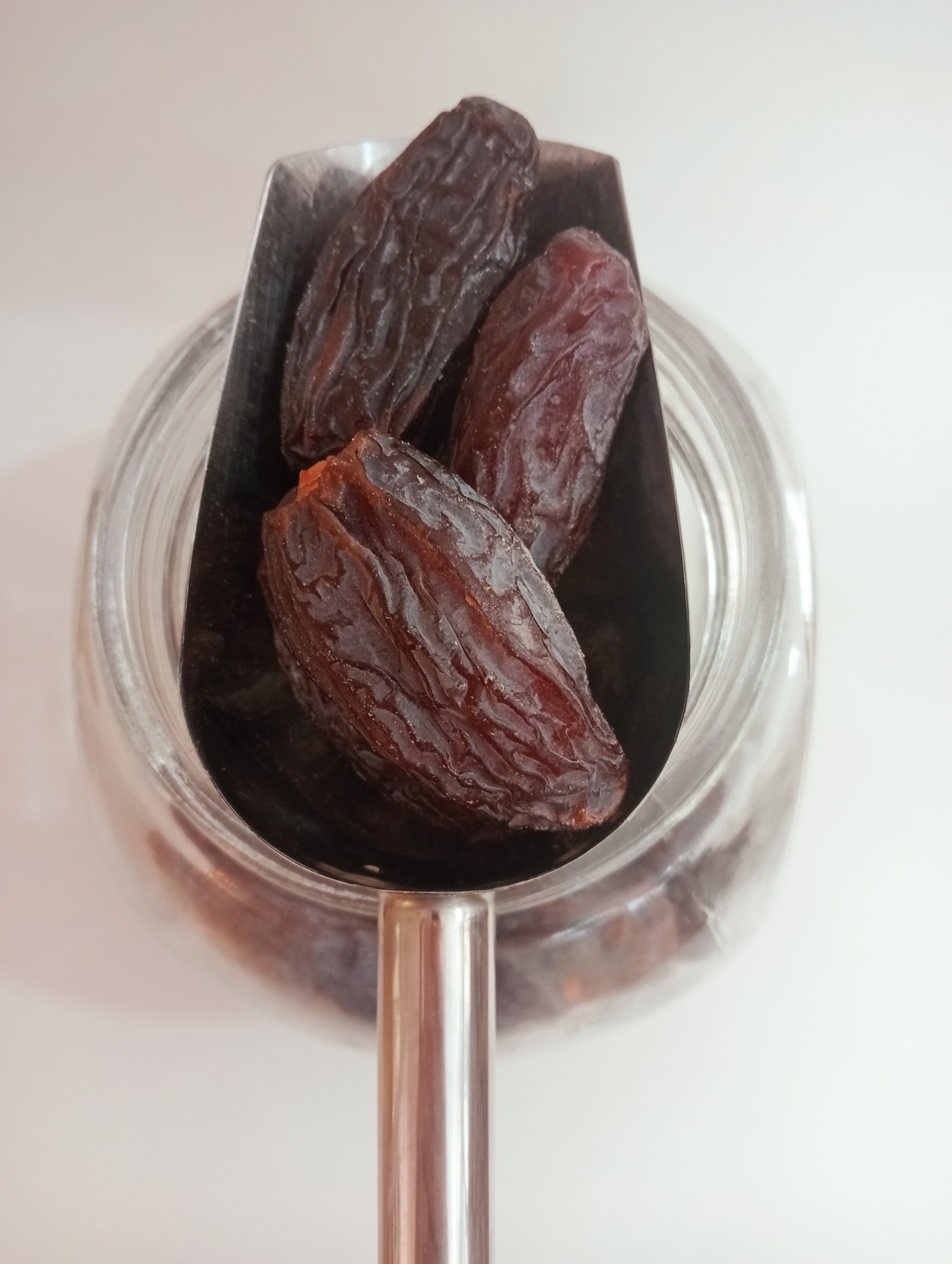 Tâmaras Medjool GRANEL Colher metálica com tâmaras sobre frasco de vidro