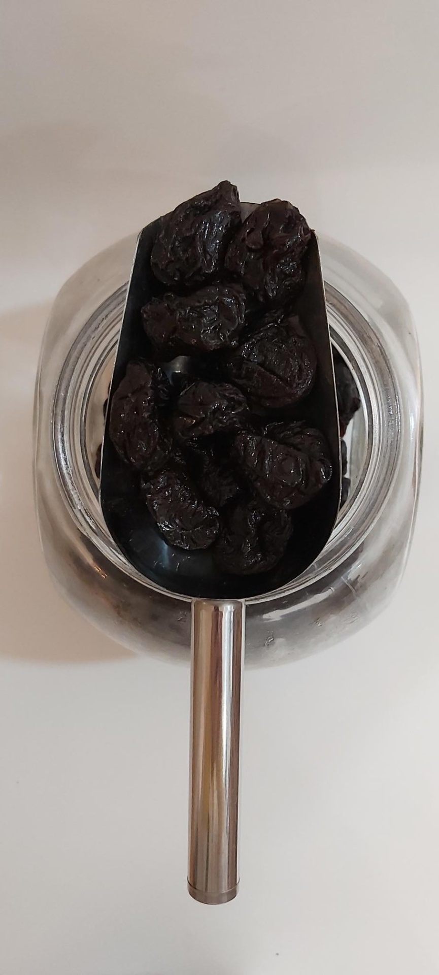 Ameixa Seca GRANEL Colher metálica com ameixas secas sobre frasco de vidro