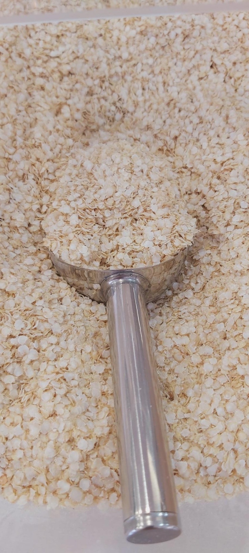 Flocos de Quinoa GRANEL Colher metálica cheia de flocos de aveia crus sobre uma superfície coberta com flocos de aveia