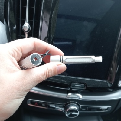 Mão segurando suporte metálico branco para caneta dentro de carro