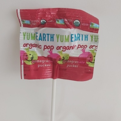 Pirulito YumEarth com embalagem vermelha e branca, texto e imagens de romãs.