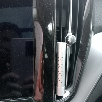 Peça metálica cilíndrica dentro da ventoinha de ar de carro ao lado do ecrã de infotainment