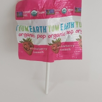 Pirulito com embalagem rosa e branca com morangos sorridentes e texto Yum Earth organic pop strawberry smash