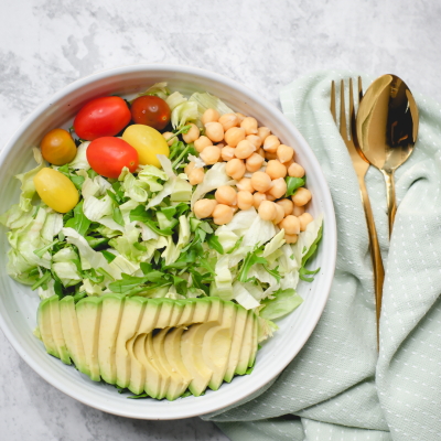 Tigela branca com salada variada e talheres dourados sobre guardanapo verde