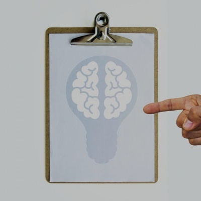Prancheta com papel mostrando desenho de lâmpada com cérebro, mão apontando