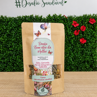 Pacote de tisana com etiqueta colorida em fundo de mesa de madeira, parede branca e plantas verdes com flores vermelhas