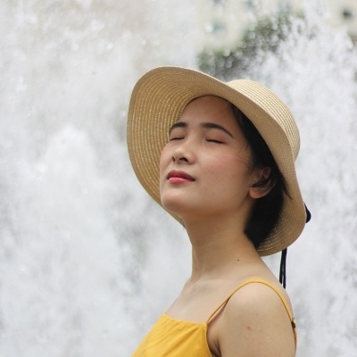 Mulher com vestido amarelo e chapéu de palha junto a uma fonte de água