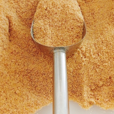 Colher metálica cheia de farinha castanho-claro sobre superfície branca