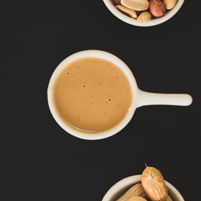 Três tigelas brancas com amendoins e pasta de amendoim em fundo preto