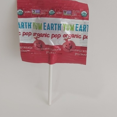 Pirulito embalado com design colorido vermelho e branco, textos EARTH YUM, e imagens de romãs