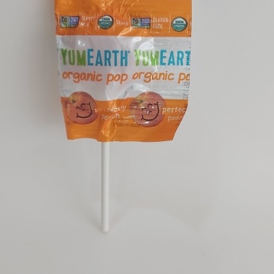 Piruleta YumEarth Organic Pop embalagem laranja e branco com pêssegos desenhados