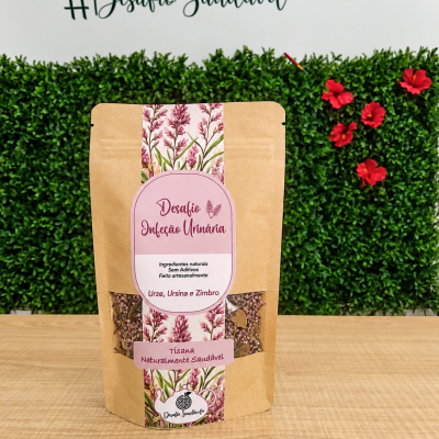Embalagem de tisana Desafio Infecção Urinária com rótulo rosa e ilustrações florais em mesa de madeira com fundo verde e flores vermelhas