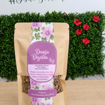 Embalagem de tisana Desafio Digestão com etiqueta violeta e decoração floral sobre mesa de madeira, fundo plantas e flores vermelhas
