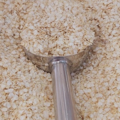 Colher metálica cheia de flocos de aveia crus sobre uma superfície coberta com flocos de aveia