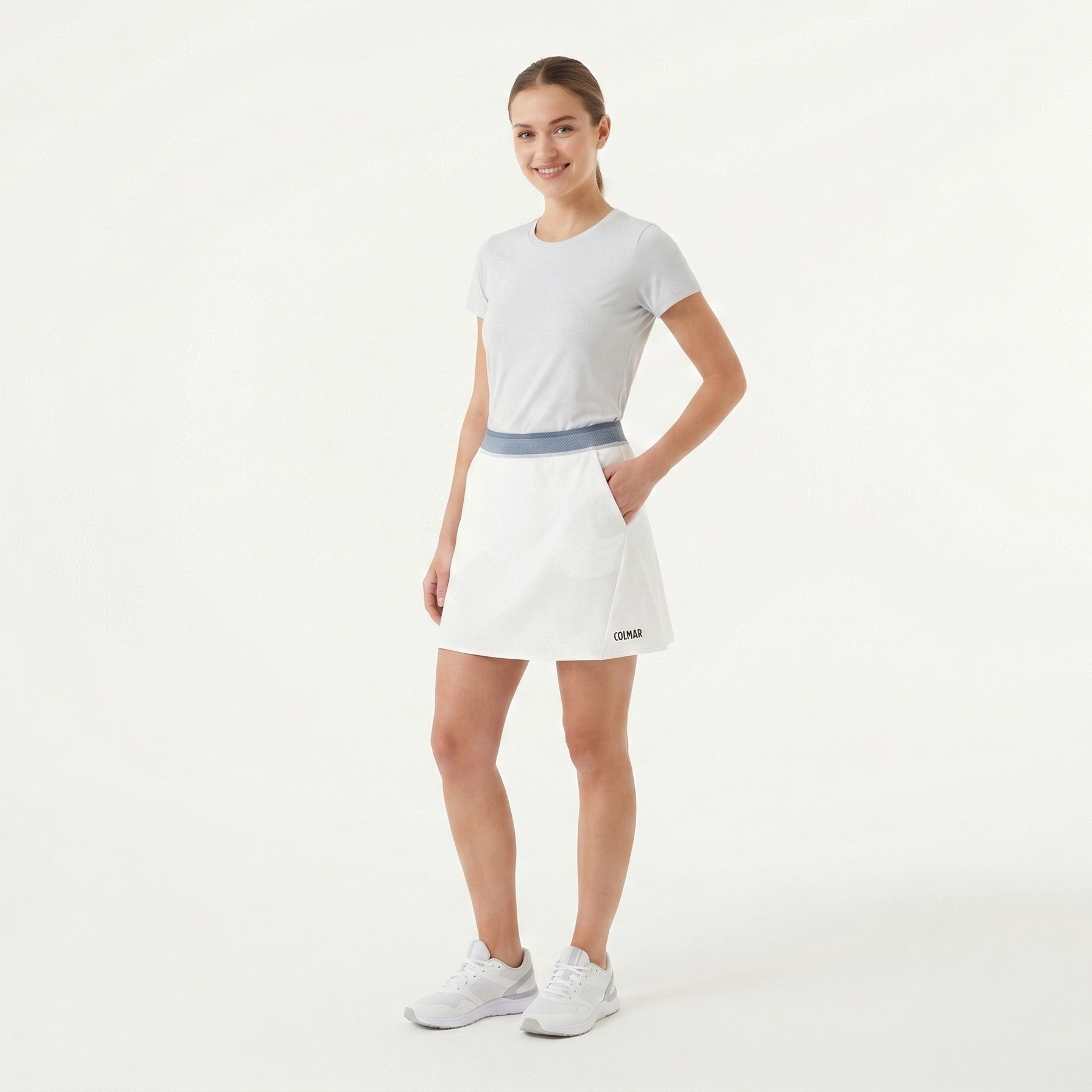 Mulher de camiseta branca e saia branca com cintura azul clara em fundo branco