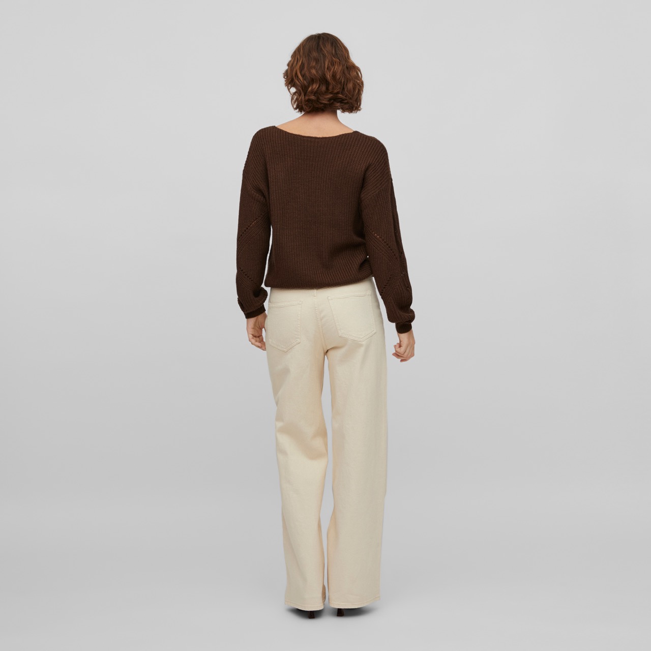 Pessoa vista pelas costas com camisola castanha escura e calças creme 