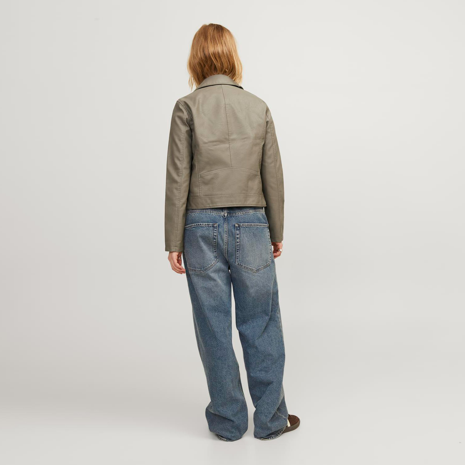 Pessoa de costas com jaqueta verde-oliva e calças de ganga azuis largas