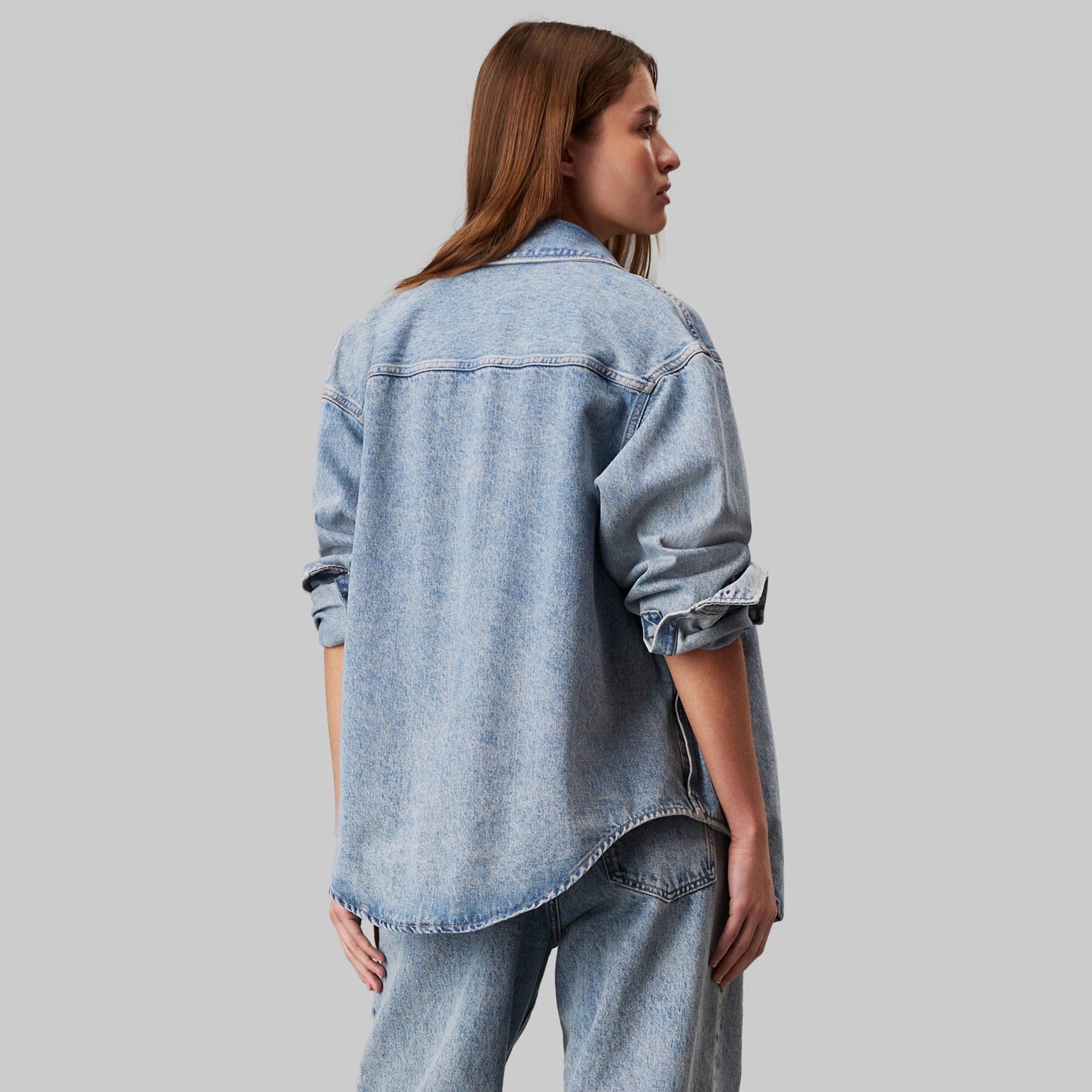 Mulher veste camisa denim azul clara e calças jeans vista de costas