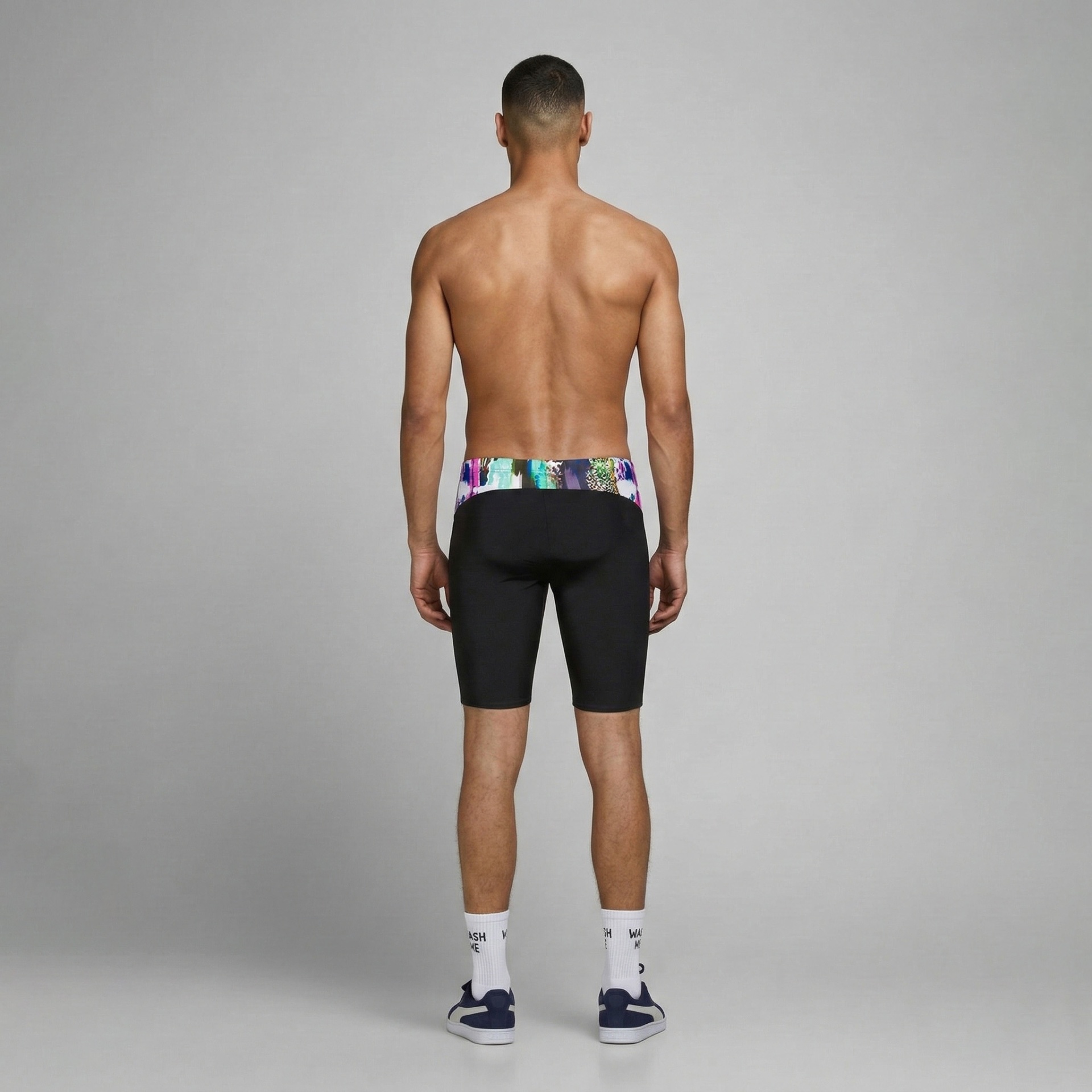 Homem de costas a usar calções justos pretos com cós multicolorido, meias brancas com texto e ténis azul e branco