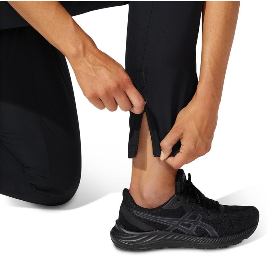 Pessoa a fechar fecho de calça preta com ténis preto num fundo branco