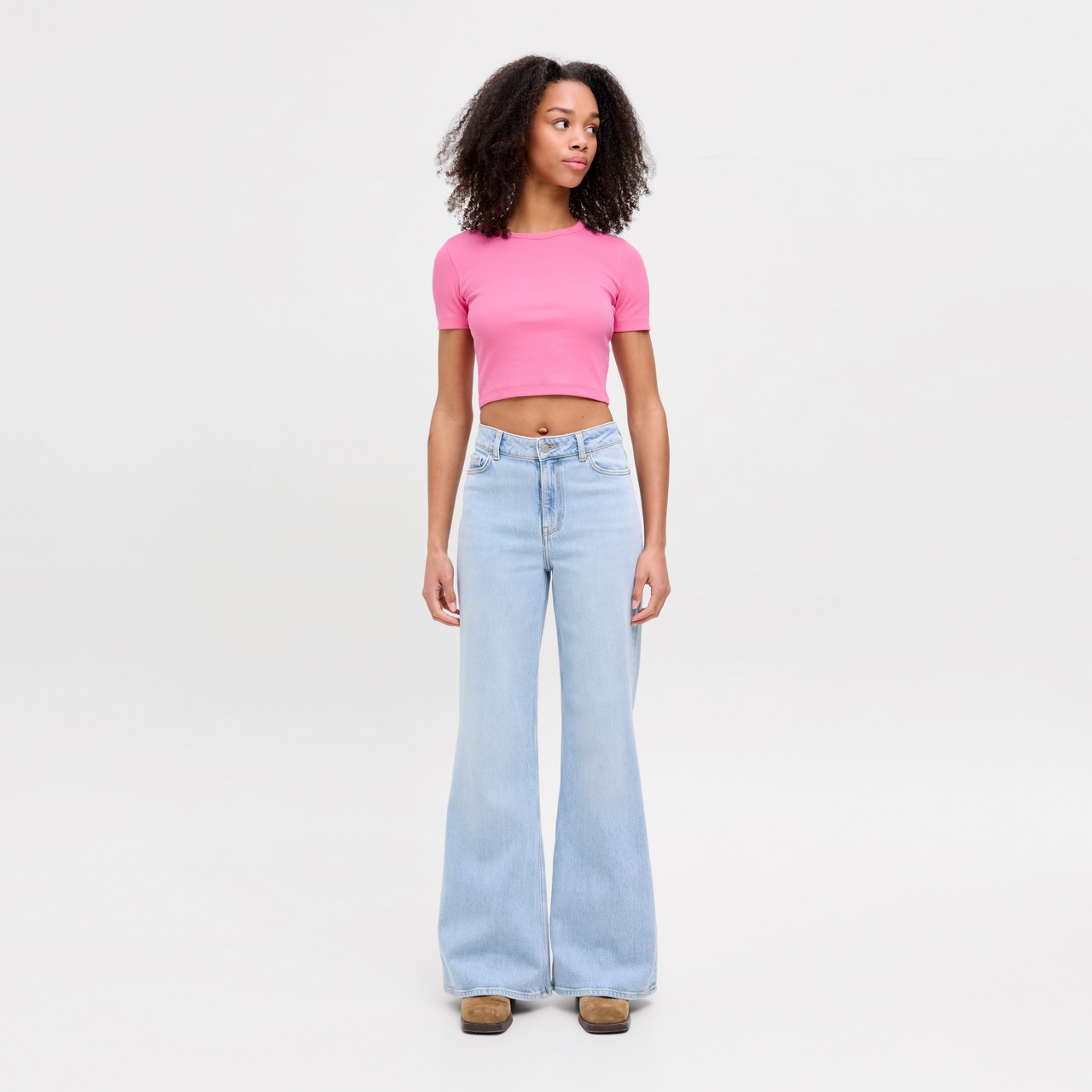 Mulher com t-shirt rosa e calças de ganga largas em fundo branco