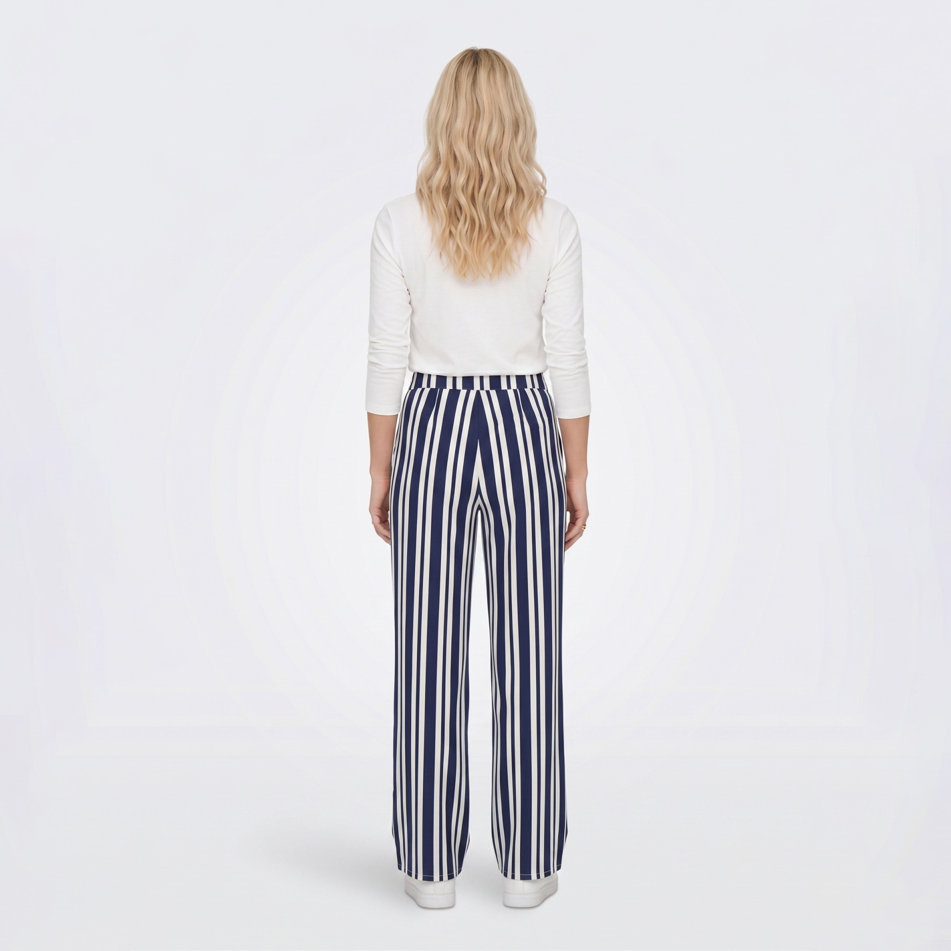 Mulher de costas com camisola branca e calças de riscas azuis e brancas.