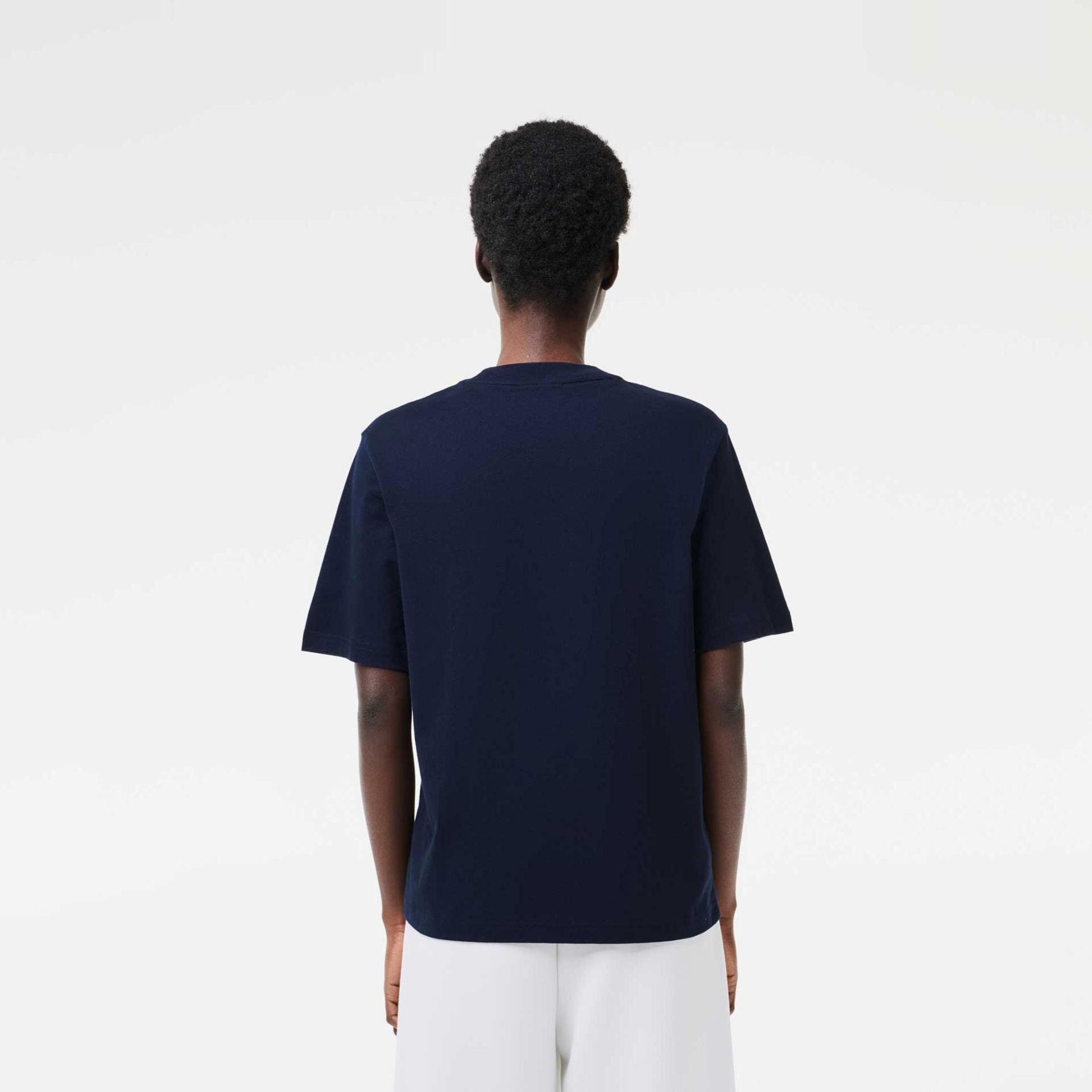 Pessoa de costas com t-shirt azul escuro e calças brancas