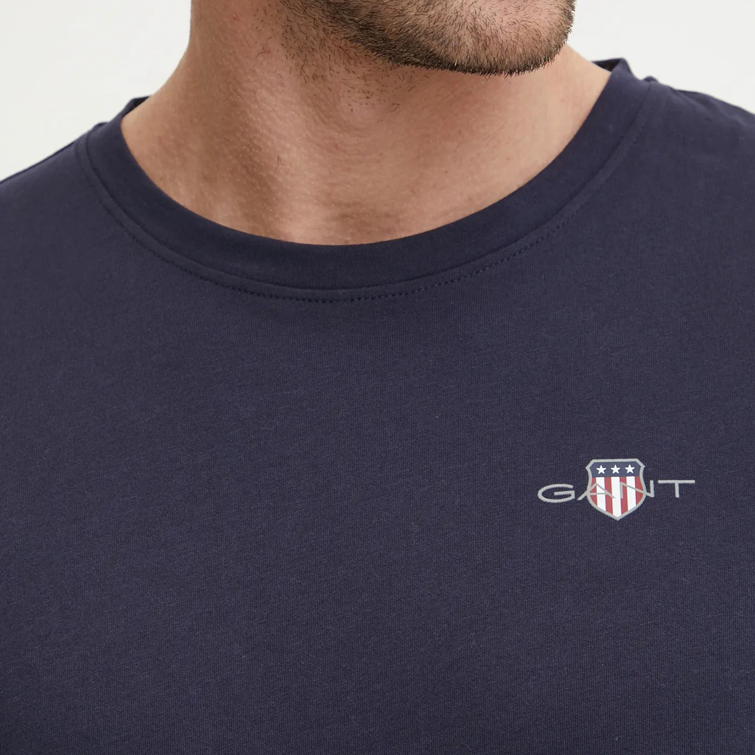 T-shirt azul escuro com logo GANT e escudo estampado na parte esquerda do peito.