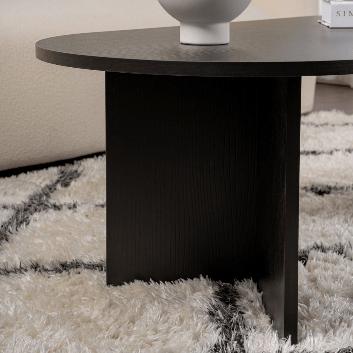 Mesa de centro preta redonda com vaso branco sobre tapete felpudo