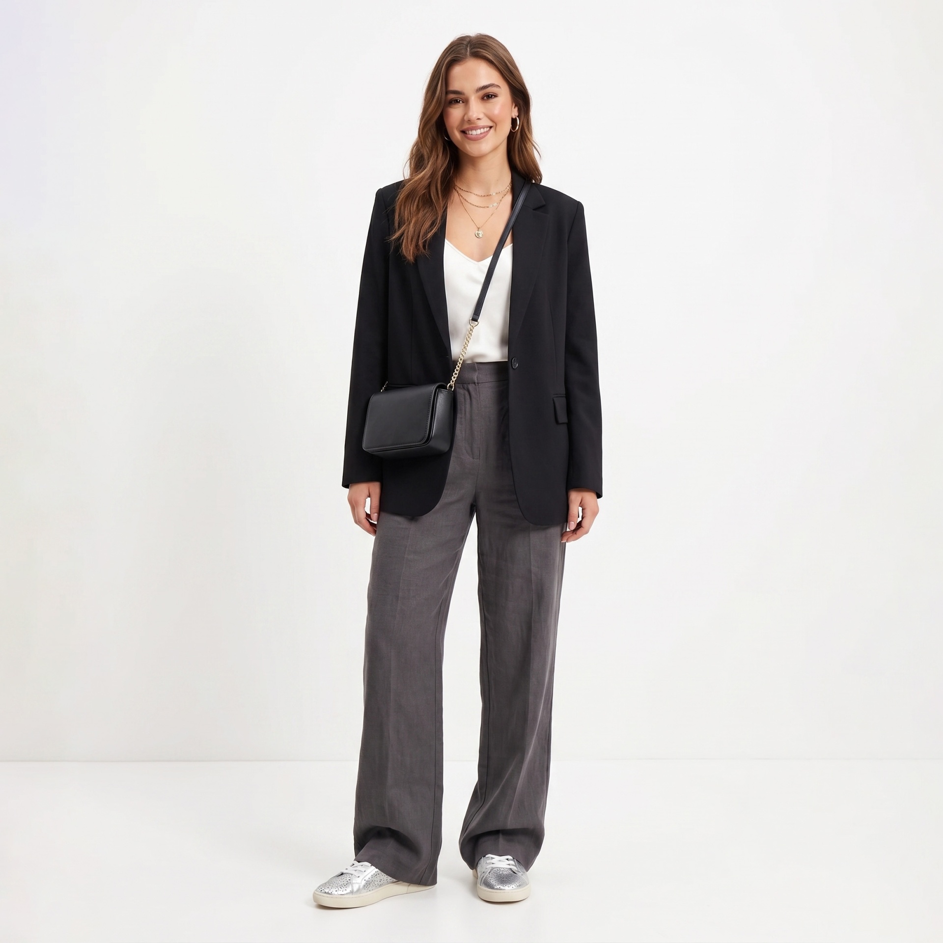 Mulher com blazer preto, camisa branca, calças cinza, sapatilhas prateadas e bolsa preta.