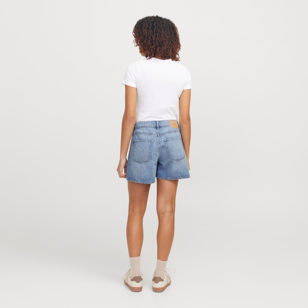 Mulher de costas com t-shirt branca e calções de ganga azuis em fundo branco